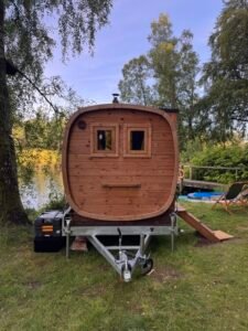 Sauna móvil exterior tonel en remolque 85 Vista frontal de la sauna móvil TimberIN Nordic Square sobre remolque junto a un lago