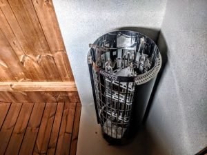 TimberIN Nordic Oval™ Terrace – interior: estufa eléctrica para sauna con cesta de piedras de acero inoxidable junto al banco