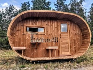 TimberIN Nordic Oval™ Terrace – sauna de exterior, vista frontal: fachada de madera termotratada con puerta acristalada, ventana lateral y porche cubierto con asientos abatibles y mesita, pinos al fondo