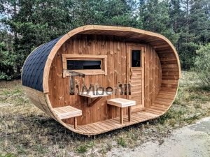 TimberIN Nordic Oval™ Terrace – sauna de exterior, vista de tres cuartos: cubierta de tejas negras, fachada de madera termotratada y porche cubierto con asientos abatibles y mesita