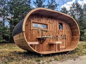 TimberIN Nordic Oval™ Terrace – sauna de exterior, vista de tres cuartos: cubierta de tejas negras, fachada de madera termotratada y porche cubierto con asientos abatibles y mesita