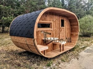 TimberIN Nordic Oval™ Terrace – sauna de exterior, vista de tres cuartos: cubierta de tejas negras, fachada de madera termotratada y porche cubierto con asientos abatibles y mesita