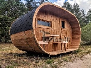 TimberIN Nordic Oval™ Terrace – sauna de exterior, vista de tres cuartos: cubierta de tejas negras, fachada de madera termotratada y porche cubierto con asientos abatibles y mesita