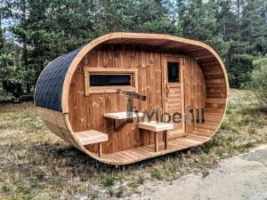 TimberIN Nordic Oval™ Terrace – sauna de exterior, vista de tres cuartos: cubierta de tejas negras, fachada de madera termotratada y porche cubierto con asientos abatibles y mesita