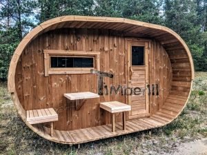 TimberIN Nordic Oval™ Terrace – sauna de exterior, vista frontal: fachada de madera termotratada con puerta acristalada, ventana lateral y porche cubierto con asientos abatibles y mesita, pinos al fondo