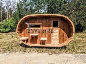 TimberIN Nordic Oval™ Terrace – sauna de exterior, vista frontal: fachada de madera termotratada con puerta acristalada, ventana lateral y porche cubierto con asientos abatibles y mesita, pinos al fondo