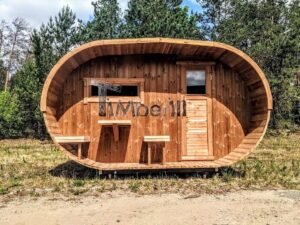 TimberIN Nordic Oval™ Terrace – sauna de exterior, vista frontal: fachada de madera termotratada con puerta acristalada, ventana lateral y porche cubierto con asientos abatibles y mesita, pinos al fondo