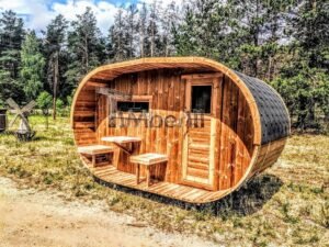 TimberIN Nordic Oval™ Terrace – sauna de exterior, vista de tres cuartos: cubierta de tejas negras, fachada de madera termotratada y porche cubierto con asientos abatibles y mesita