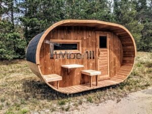 TimberIN Nordic Oval™ Terrace – sauna de exterior, vista de tres cuartos: cubierta de tejas negras, fachada de madera termotratada y porche cubierto con asientos abatibles y mesita