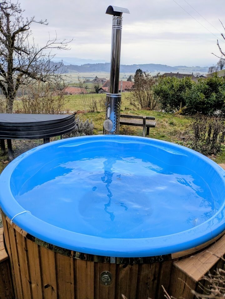 Jacuzzi con cubeta azul lisa lleno de agua y chimenea de acero, con vistas al campo