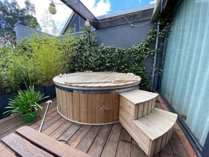 Jacuzzi de madera con cubierta y escalera sobre una plataforma entre las plantas de un jardín