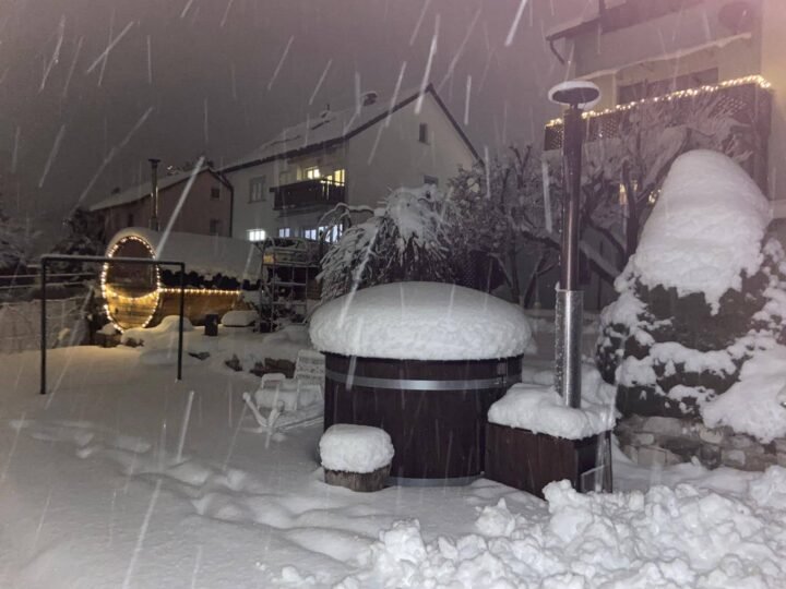 Jacuzzi con cubierta en un jardín nevado durante una nevada nocturna