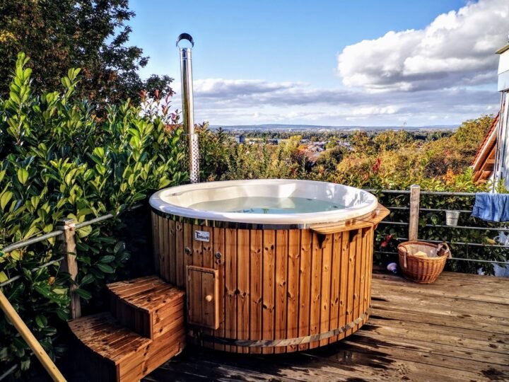 Jacuzzi exterior de madera con escalera y chimenea en una terraza con vistas a las colinas