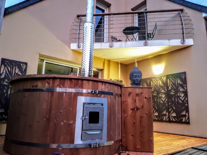Jacuzzi de madera con estufa de leña y chimenea en una terraza iluminada por la noche