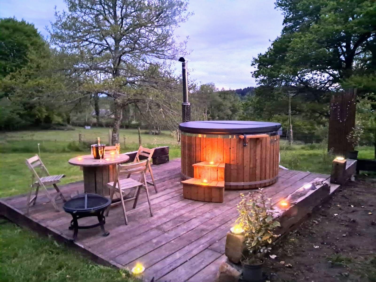 Jacuzzi de madera con estufa de leña en una terraza de madera al anochecer, con velas encendidas