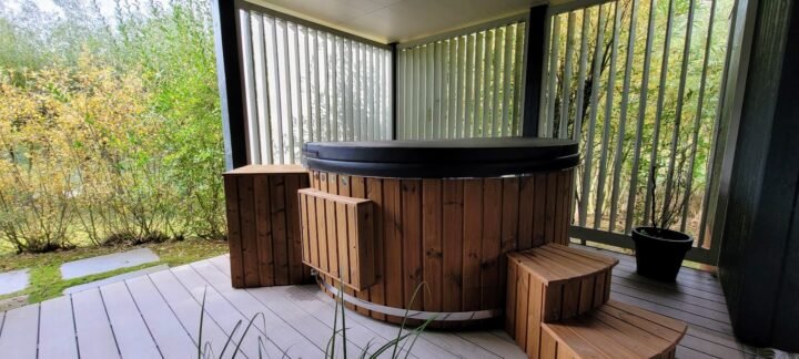 Jacuzzi redondo de madera con cubierta y caja técnica lateral, sin chimenea, en una terraza cubierta