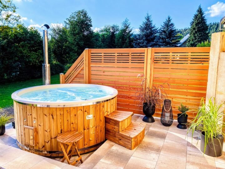 Jacuzzi redondo de madera con cubeta clara y escalera en un patio del jardín, delante de una valla de madera