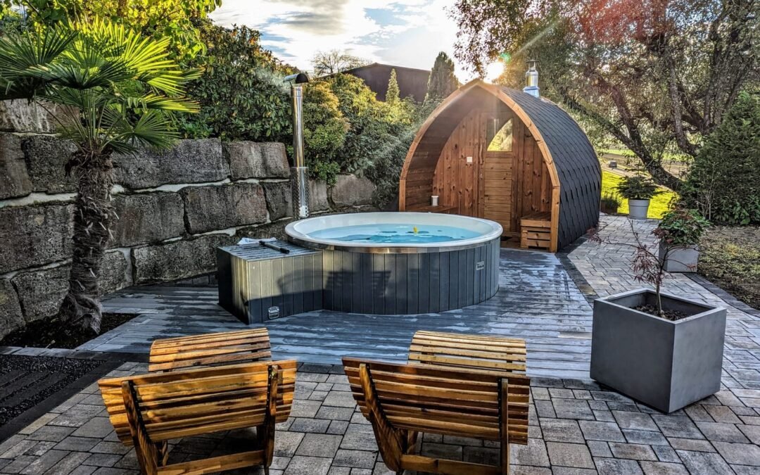 Jacuzzi exterior y sauna de madera en una terraza de piedra con dos tumbonas