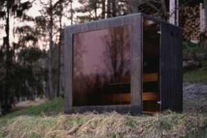 Sauna de exterior TimberIN Nordic Cube de CLT con cristal oscuro en el bosque