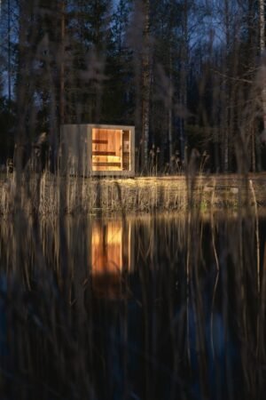 Sauna de exterior TimberIN Nordic Cube de CLT de noche entre los juncos