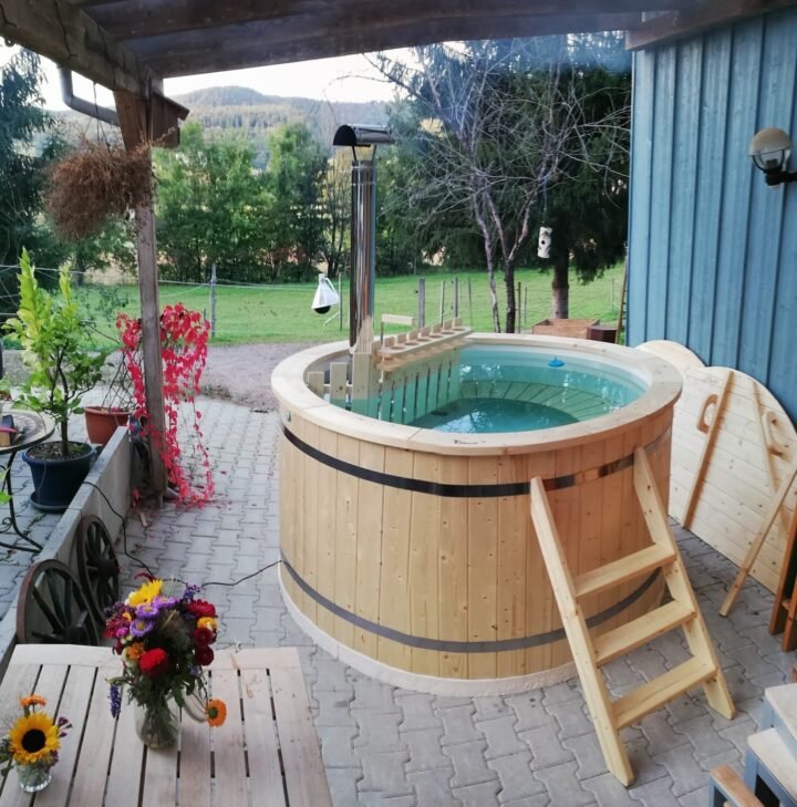 Tinaja de madera bajo una pérgola entre macetas de flores, con vistas al campo